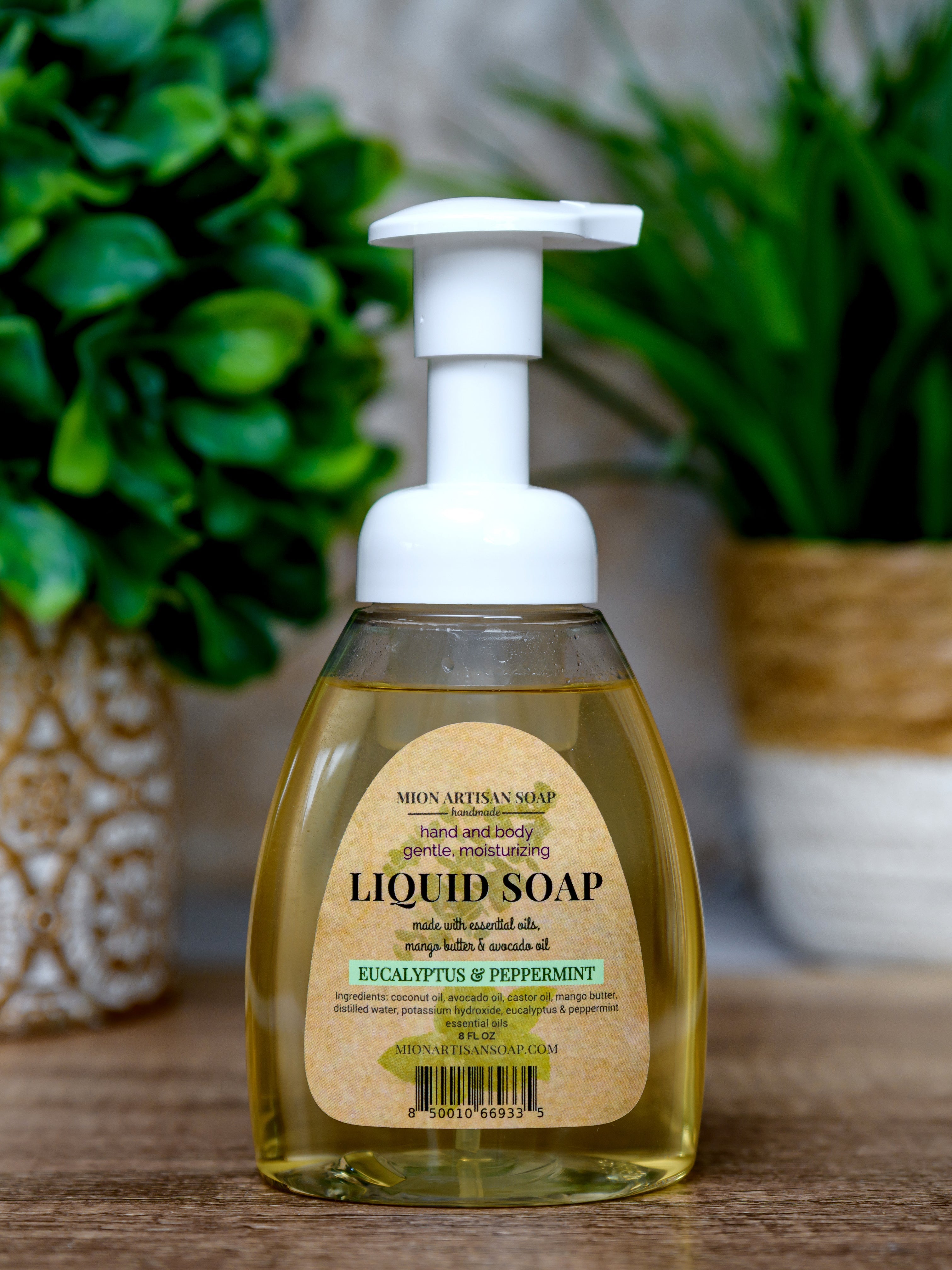 Bottle of liquid soap with a pump on a wooden surface, surrounded by green plants.